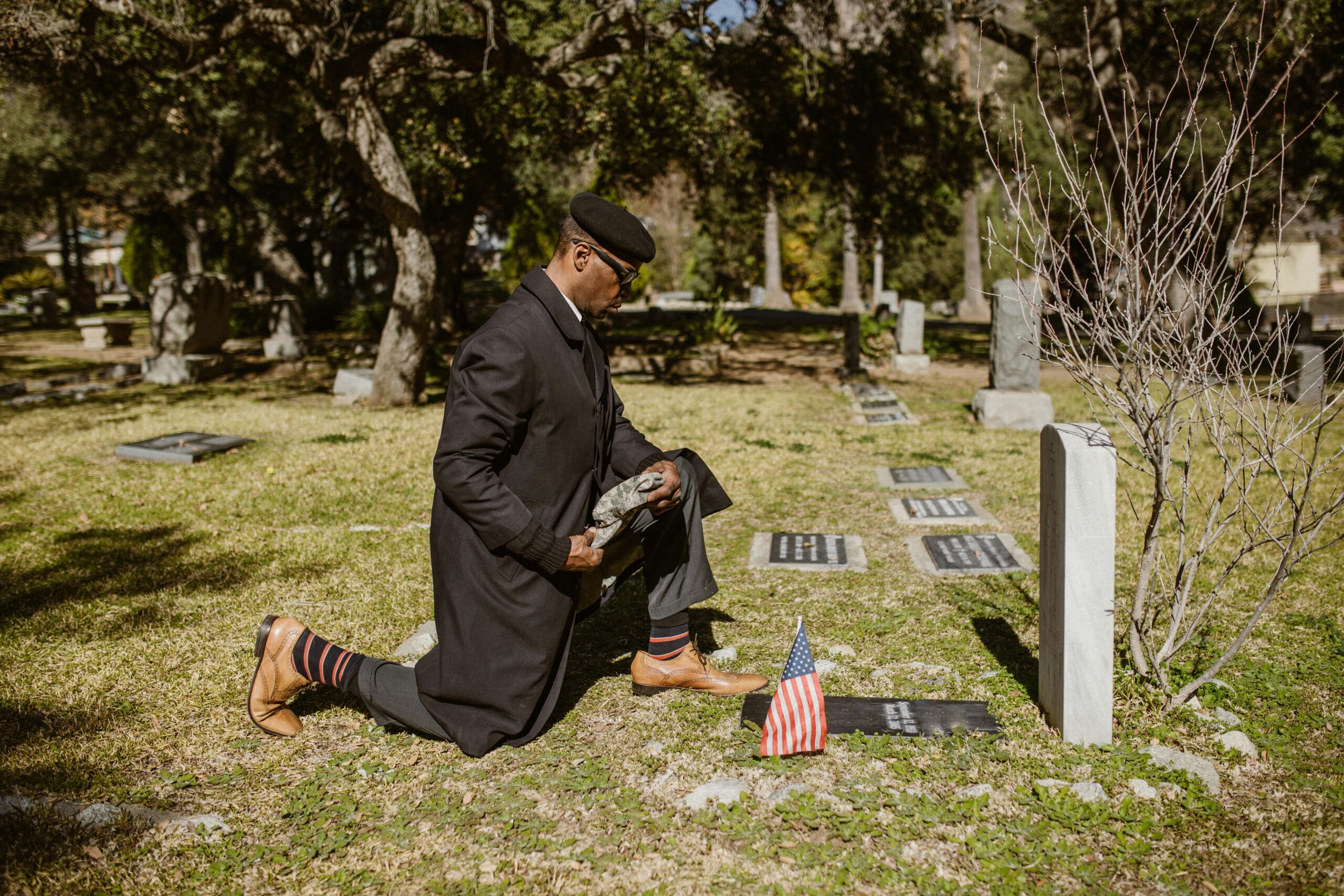 A man kneeling at a gravestone in a cemetery with an American flag.